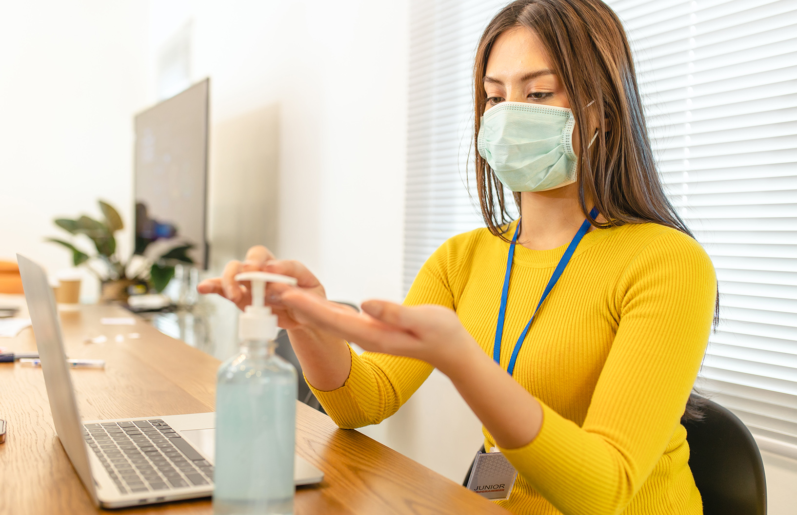 Business woman working from home wearing protective mask.Asian f Business woman working from home wearing protective mask.Asian female in quarantine for coronavirus wearing protective mask. Working from home. Cleaning her hands with sanitizer gel.Alcohol gel to prevent corona virus covid-19 infection.