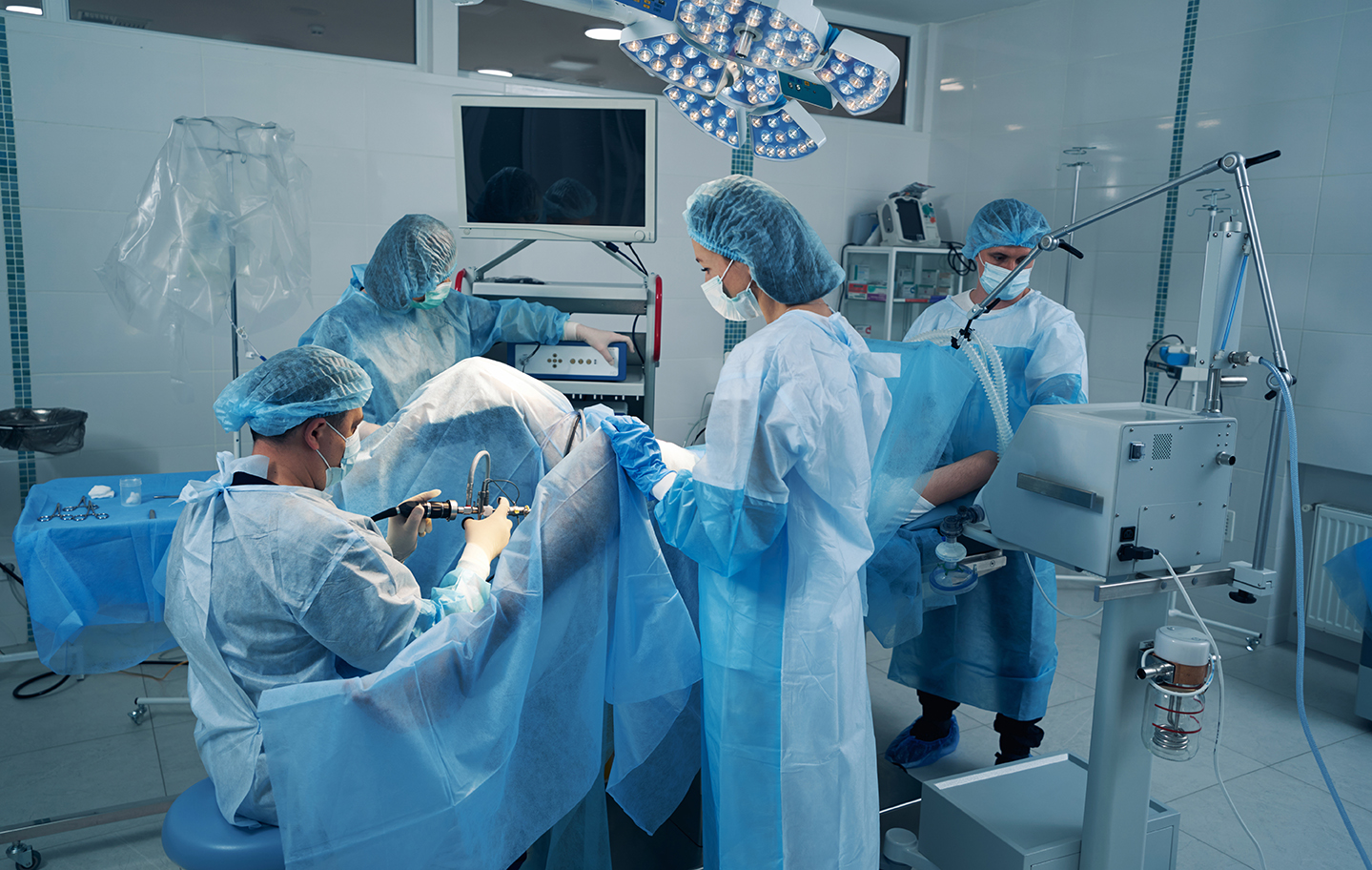 Four surgery specialist in operating theater treating patient Group of operating surgeons performing surgery on person using laparoscopic rod camera and turning on viewing screen