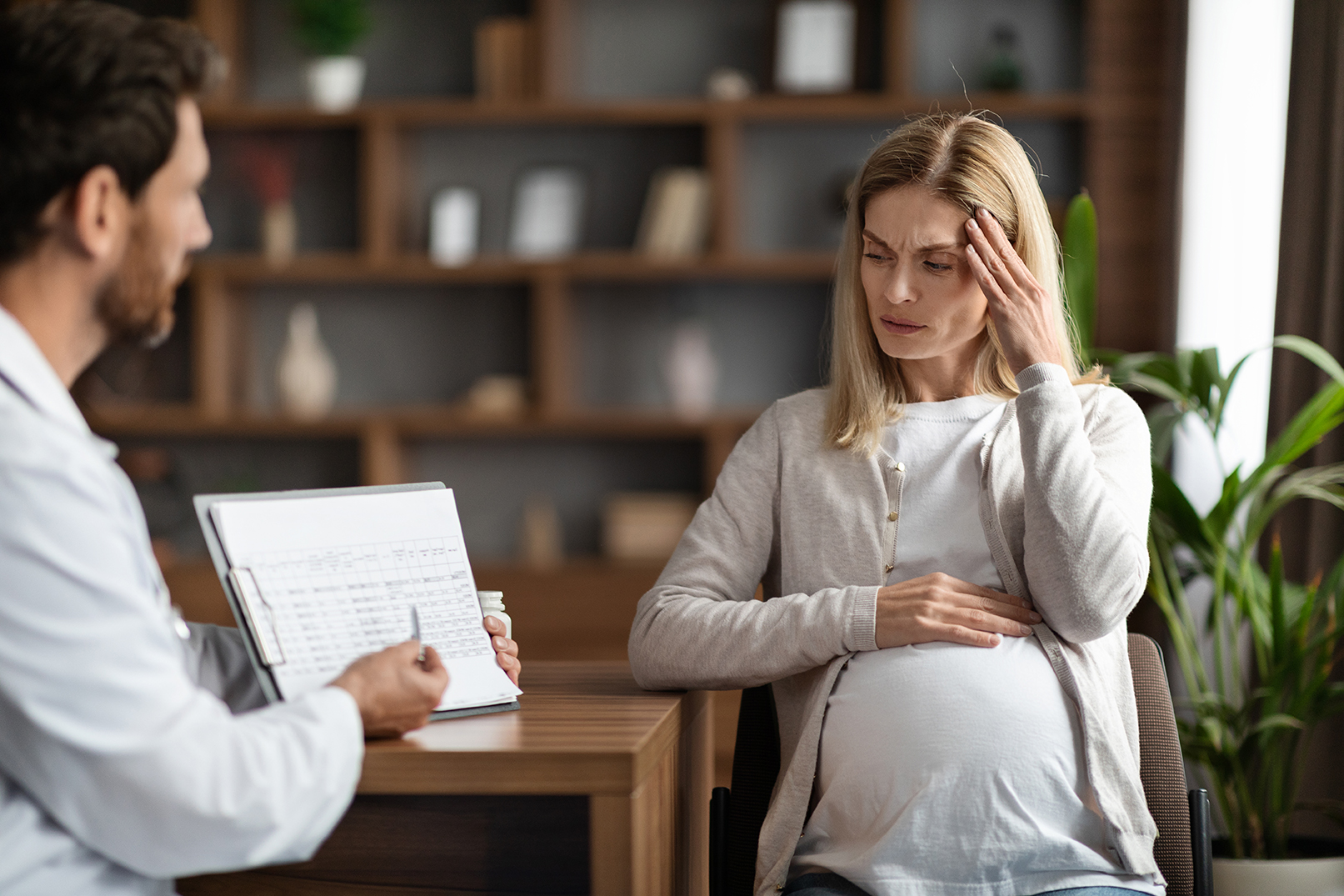 Gynecologist Doctor Showing Clipboard With Medical Test Results To Stressed Pregnant Woman Gynecologist Doctor Showing Clipboard With Medical Test Results To Stressed Pregnant Woman During Meeting In Clinic, Therapist Man Demonstrating Complete Blood Count Range To Worried Expectant Lady