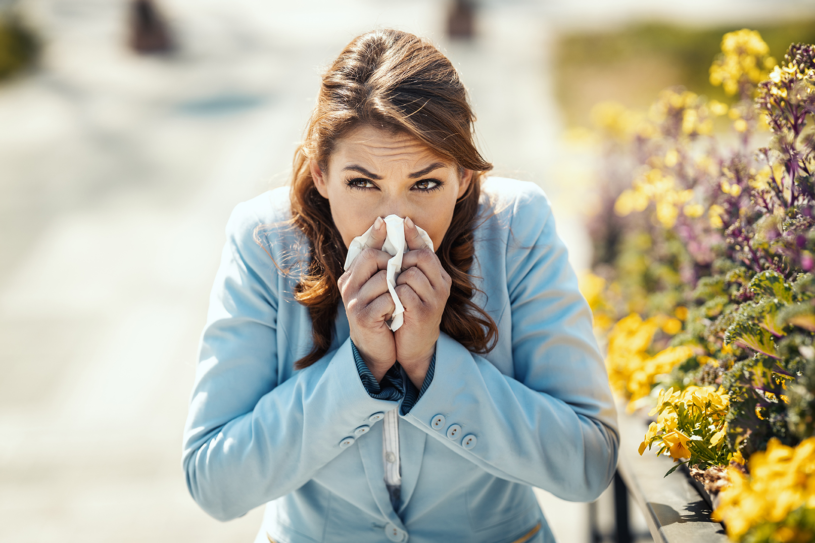 A young business woman blowing her nose out during a break outside due to allergies or colds.