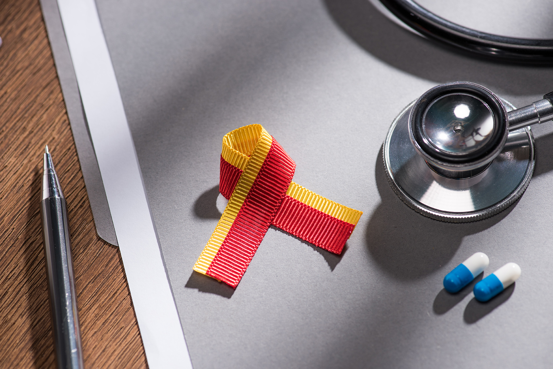 selective focus of ribbon, stethoscope, pills and folder with pe selective focus of ribbon, stethoscope, pills and folder with pen on table, world hepatitis day