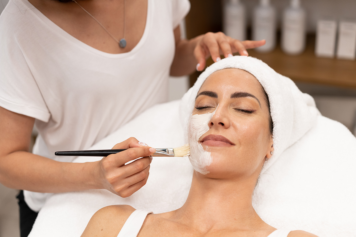 Aesthetics applying a mask to the face of a Middle-aged woman in modern wellness center. Aesthetics applying a mask to the face of a Middle-aged woman in modern wellness center. Beauty and Aesthetic concepts.