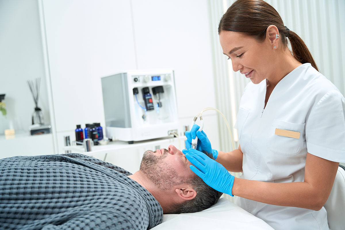 Beautician processes the forehead of a man with modern device Beautician processes the forehead of a man with modern device, the specialist uses the non-surgical microdermabrasion method in his work