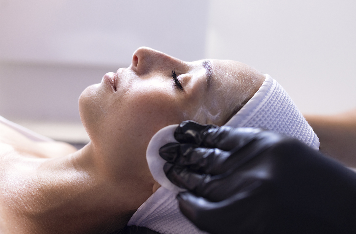 Close up of beautiful young brunette woman during facial cleansi Close up of beautiful young brunette woman during facial cleansing and massage. Cosmetic procedures in a beauty salon or clinic. Lighted candles on background. Skin care and health concept.