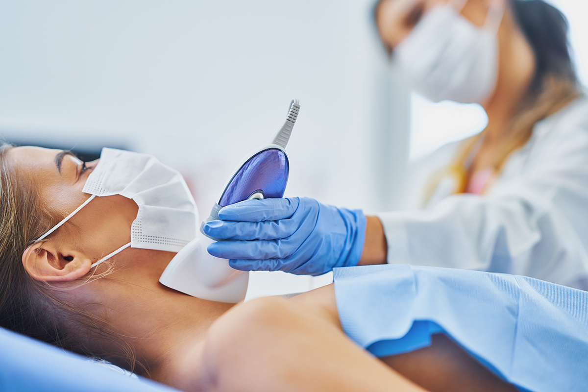 Picture of doctor checking up thyroid to her female patient wearing a mask