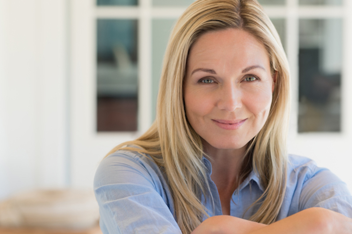 Happy mature woman relaxing on her couch at home in the living room. Close up face of senior woman looking at camera. Portrait of happy woman in blue shirt smiling.
