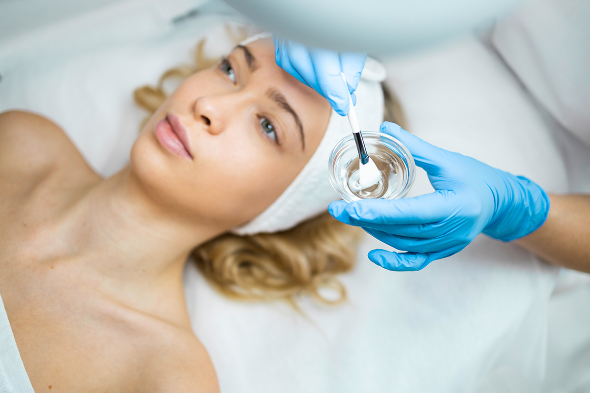 Hands of female cosmetologist applying a transparent mask with a brush on a woman face. Face skin care Hands of female cosmetologist applying a transparent mask with a brush on a woman face. Face skin care