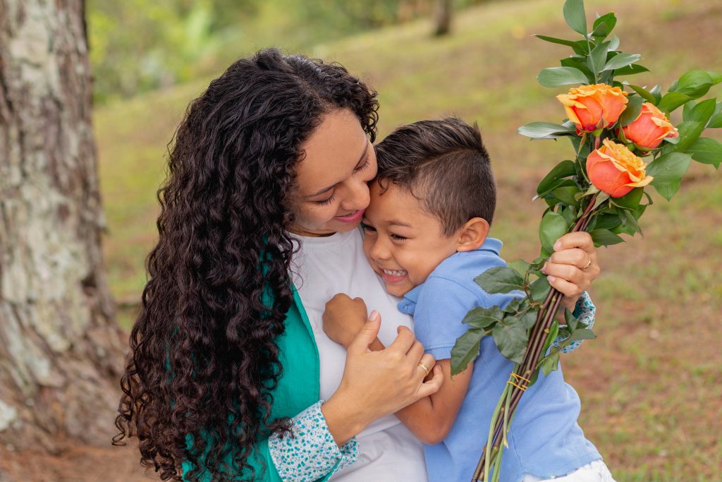 Affectionate Mother Embracing Laughing Child with Orange Roses in a Park