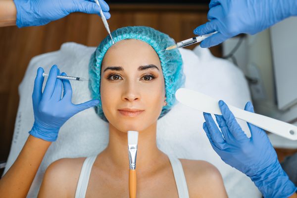 Cosmetician hands with working tools at female patient face. Rejuvenation procedure in beautician salon. Doctor and woman, cosmetic surgery against wrinkles and aging