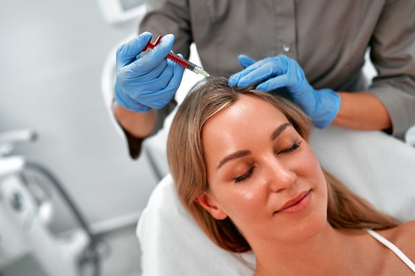 Mesotherapy, vitamin injections in head skin of hair area. Professional hair loss treatment. Close up view of woman head and doctor's hands with syringe.