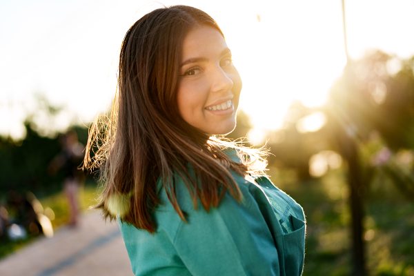 Portrait of young woman in green shirt smiling in a park, close up