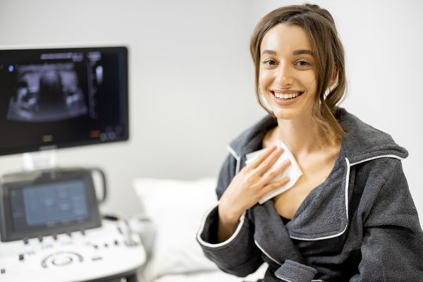Happy woman after examining thyroid with ultrasound scan in medical clinic. Health and wellness concept.